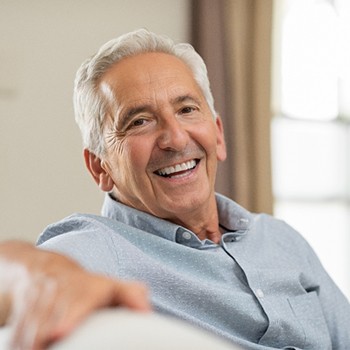 An older man sitting on a couch smiling