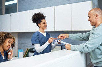 a patient handing forms back to a front desk worker