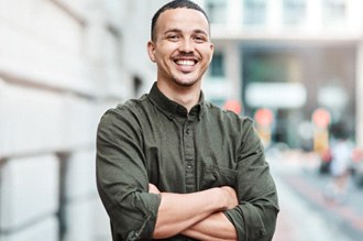 a smiling man wearing a button up shirt with his arms crossed