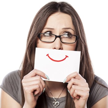 A woman holding a card with a smile drawn on it over her mouth