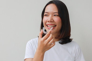 Smiling patient holding clear aligner