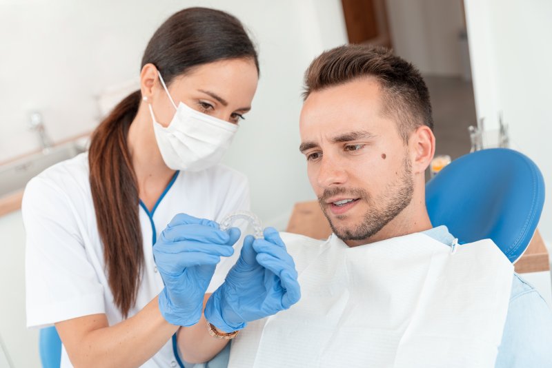 A dentist in Crown Point holding Invisalign aligners in front of a patient